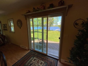 A room with a large sliding glass door leading to a patio with a view of a lake and trees. - Luck Charlie Lodge (Winter)