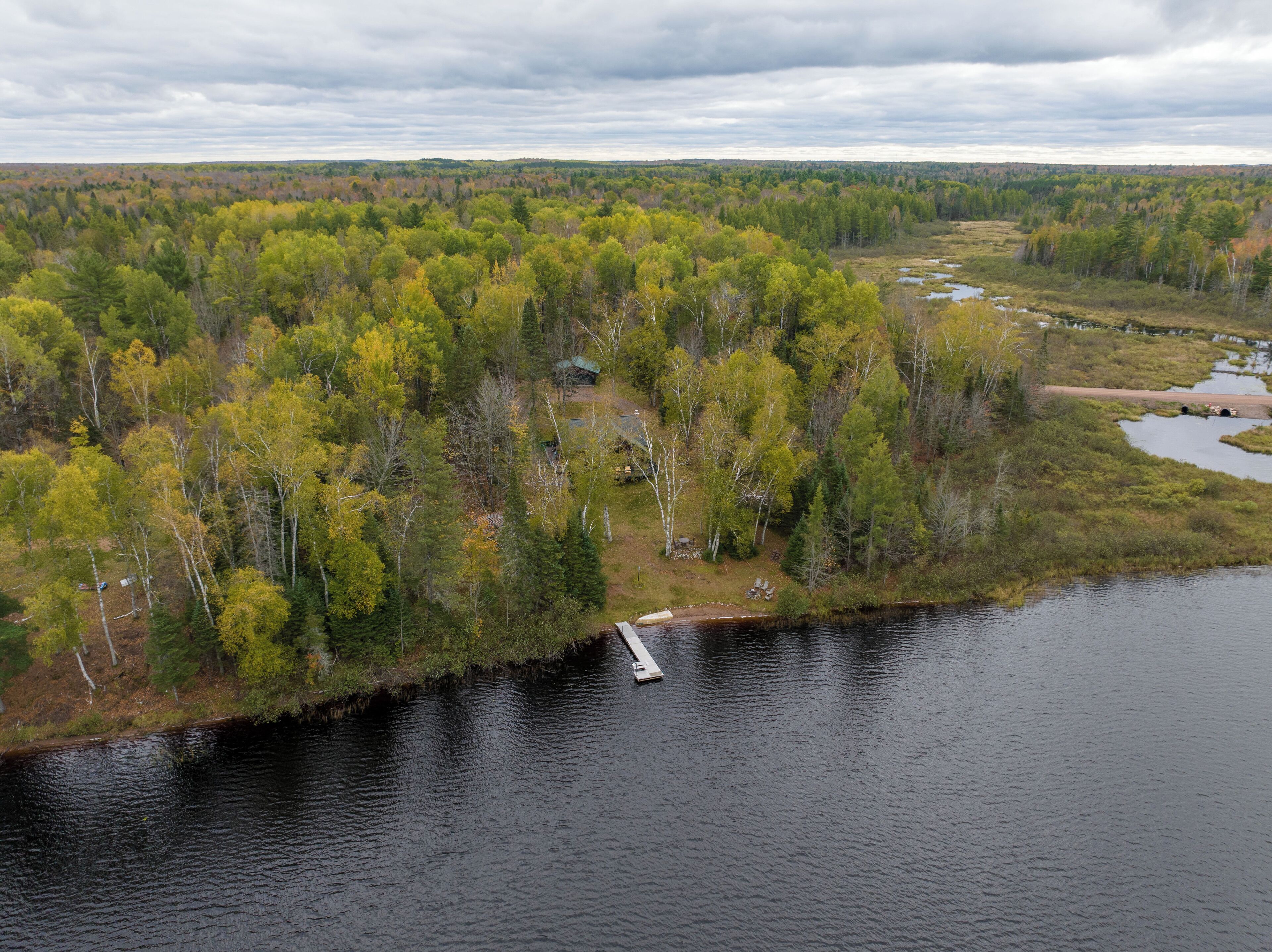 Järven rannalla sijaitseva mökki, jonka ympärillä on tiheä metsä, ja jonka edessä on laituri, joka ulottuu veteen.