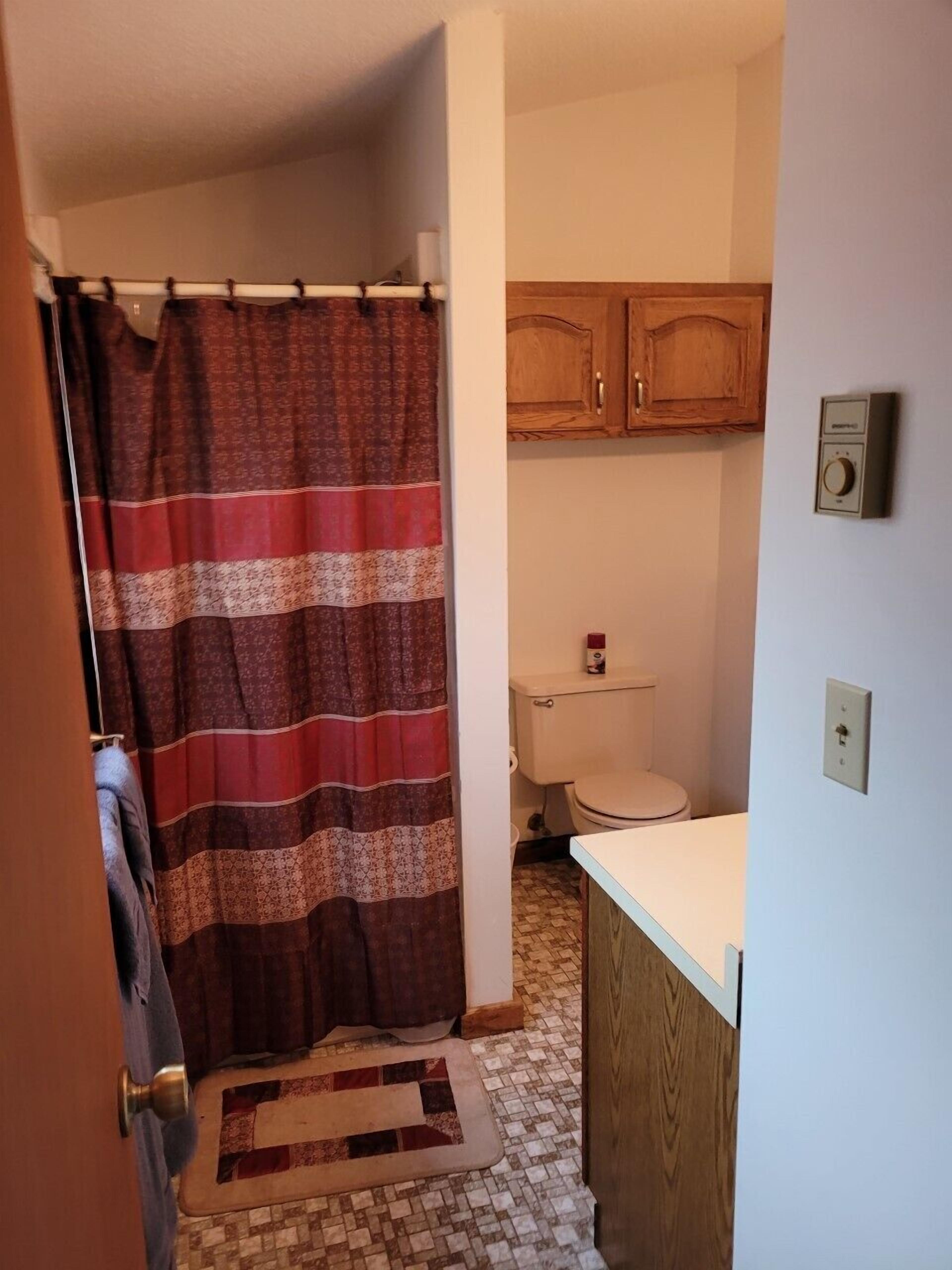 Een badkamer met douchegordijn, houten kastjes, toilet en wastafel.