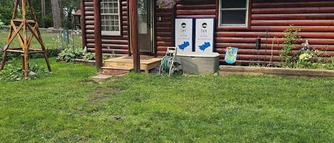 Une cabane rustique en rondins de bois, dotée d’un petit porche et d’un moulin à vent dans la cour.