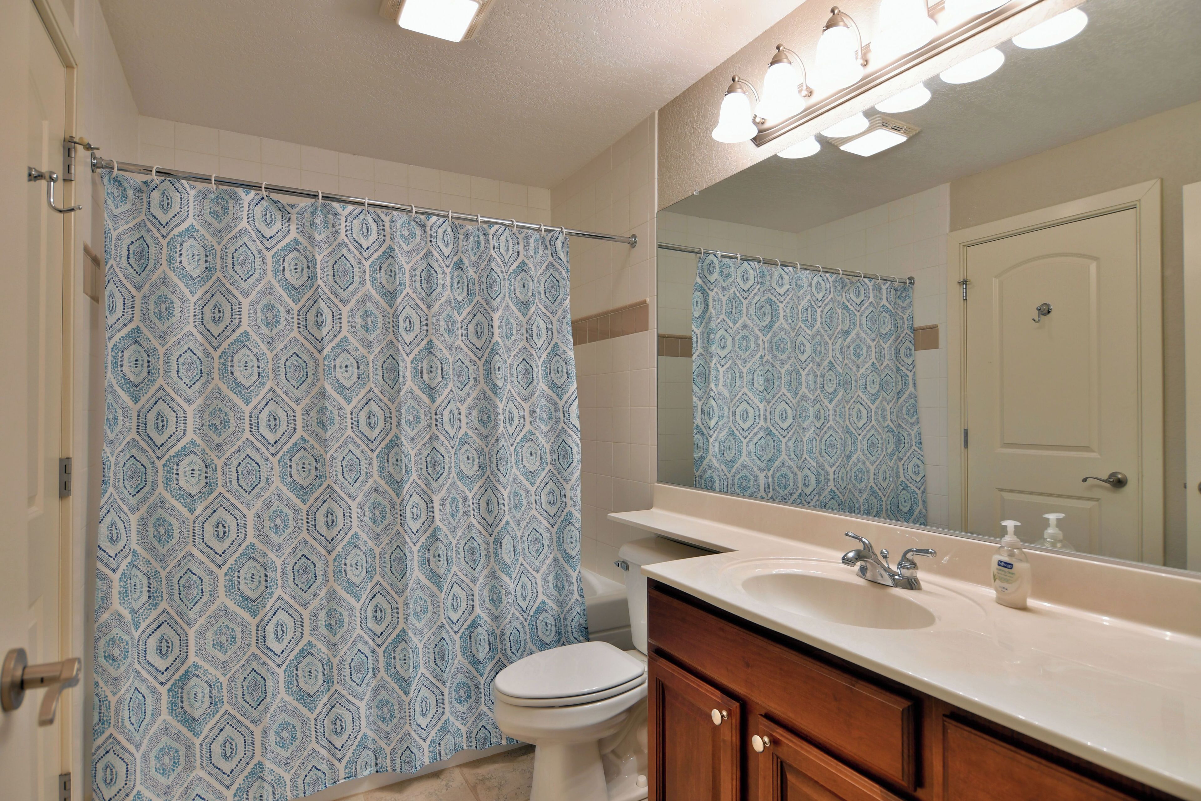 A bathroom with a patterned shower curtain, a toilet, a sink, and a mirror.