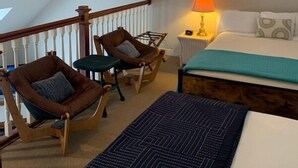 Une chambre à coucher avec un lit, un bureau, deux chaises, un ventilateur de plafond et un tableau accroché au mur.