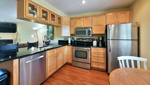 A modern kitchen with stainless steel appliances, wooden cabinets, and a black countertop. - Unit 109 2 Bdrm/ 2 BA (Birchwood)