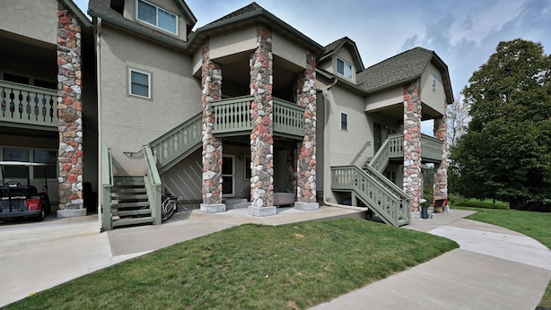 A multi-story house with stone pillars, a covered porch, and a front staircase. - Unit 109 2 Bdrm/ 2 BA (Birchwood)