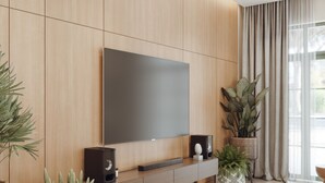 Un soggiorno moderno con un'ampia televisione a schermo piatto montata su una parete in legno, un mobile console minimalista con diffusori e diverse piante in vaso.