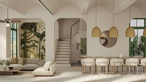 Un soggiorno moderno con divano, tavolino e zona pranzo con sedie. Si vede una scala che conduce a un altro livello, e una grande finestra con cornici verdi.