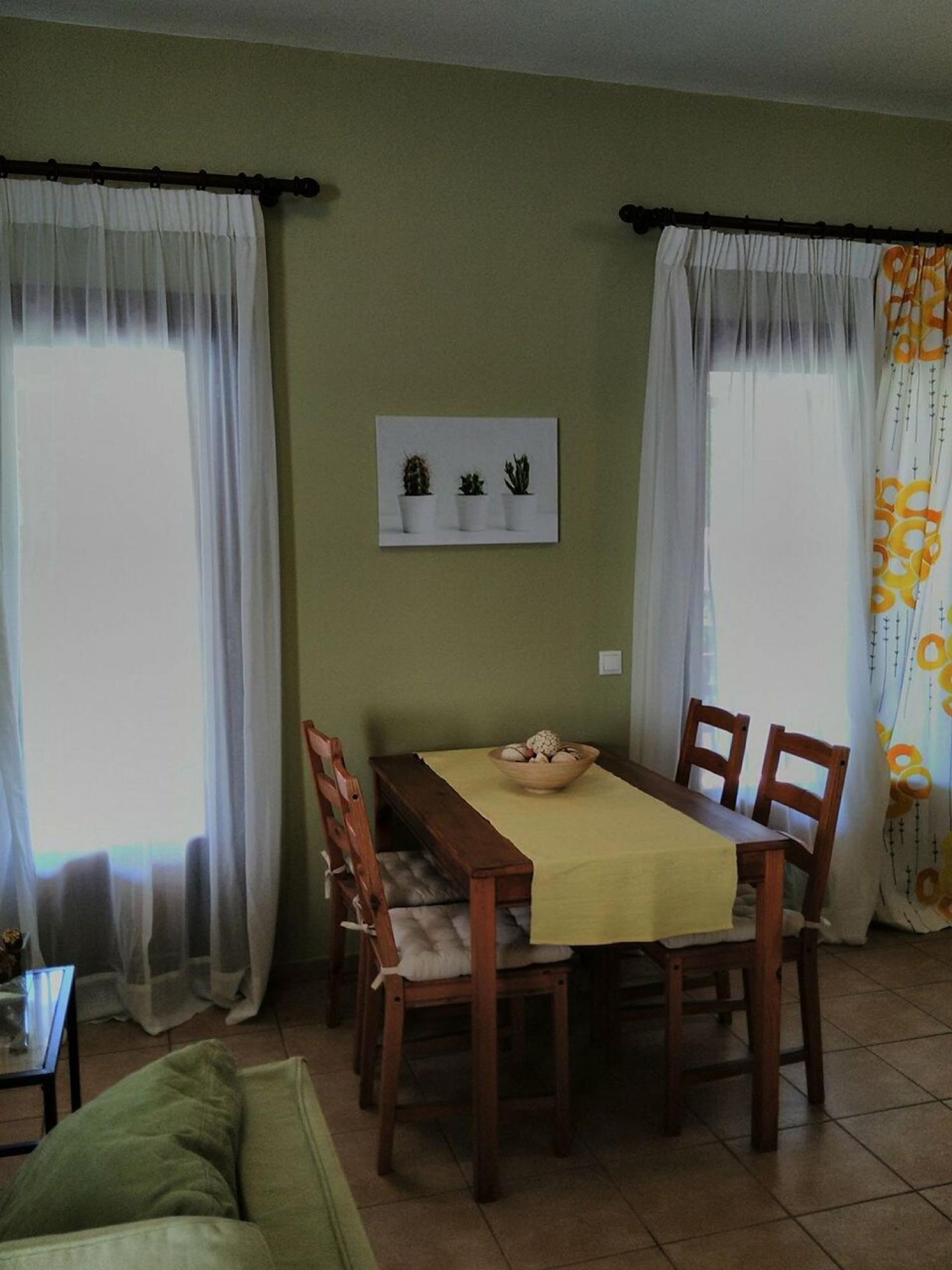 A dining area with a table set for four, a sofa, and a wall-mounted picture of three potted plants.