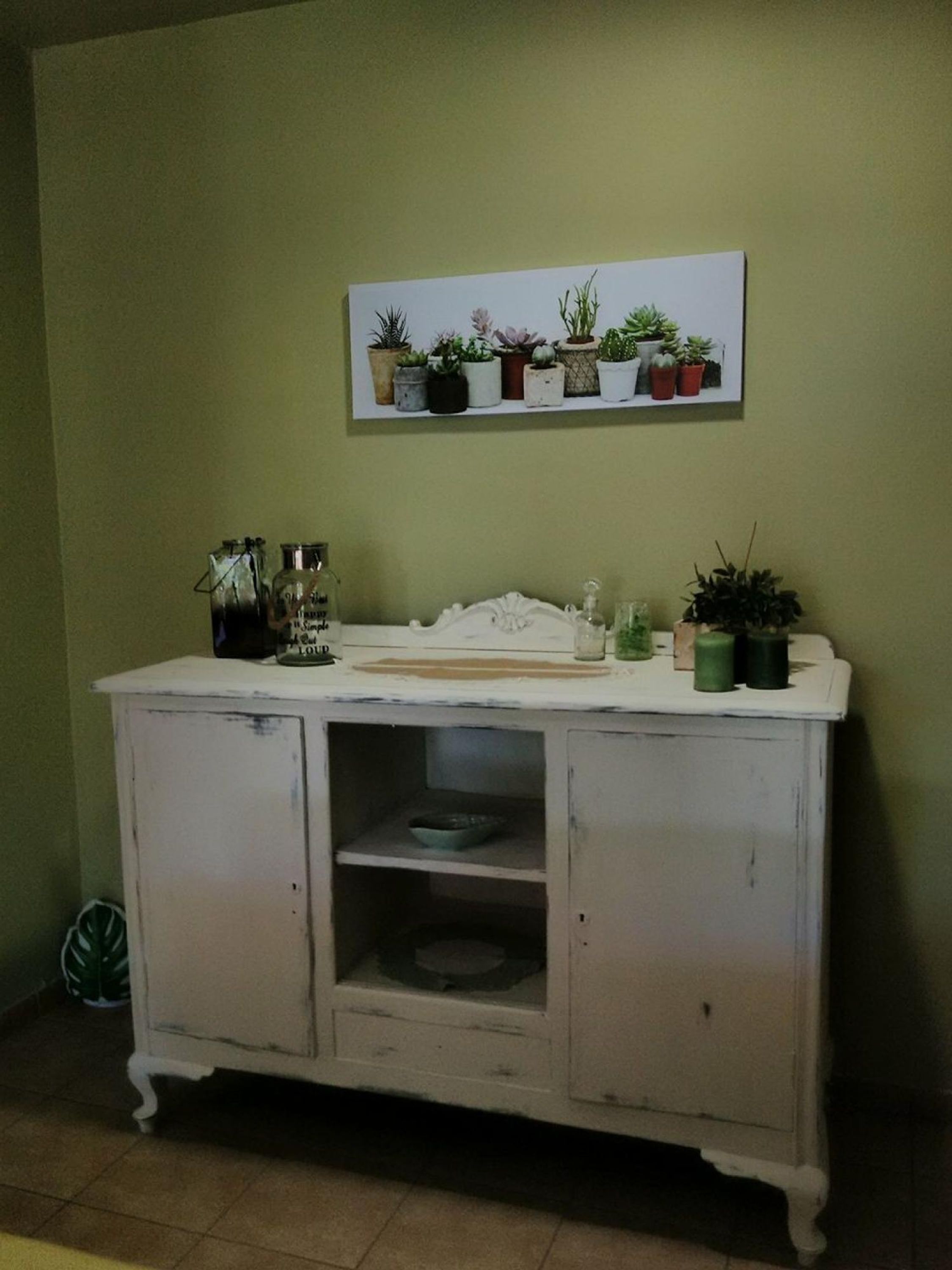 A white cabinet with a shelf above it, holding various potted plants.