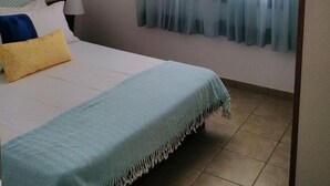 Ein Schlafzimmer mit einem Bett, einem Fenster mit durchscheinenden Vorhängen, einem Deckenventilator und einer Wand-Klimaanlage.