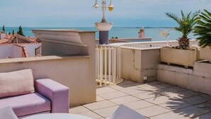 Une terrasse avec une table et des chaises blanches, un canapé rose et une vue sur la mer.