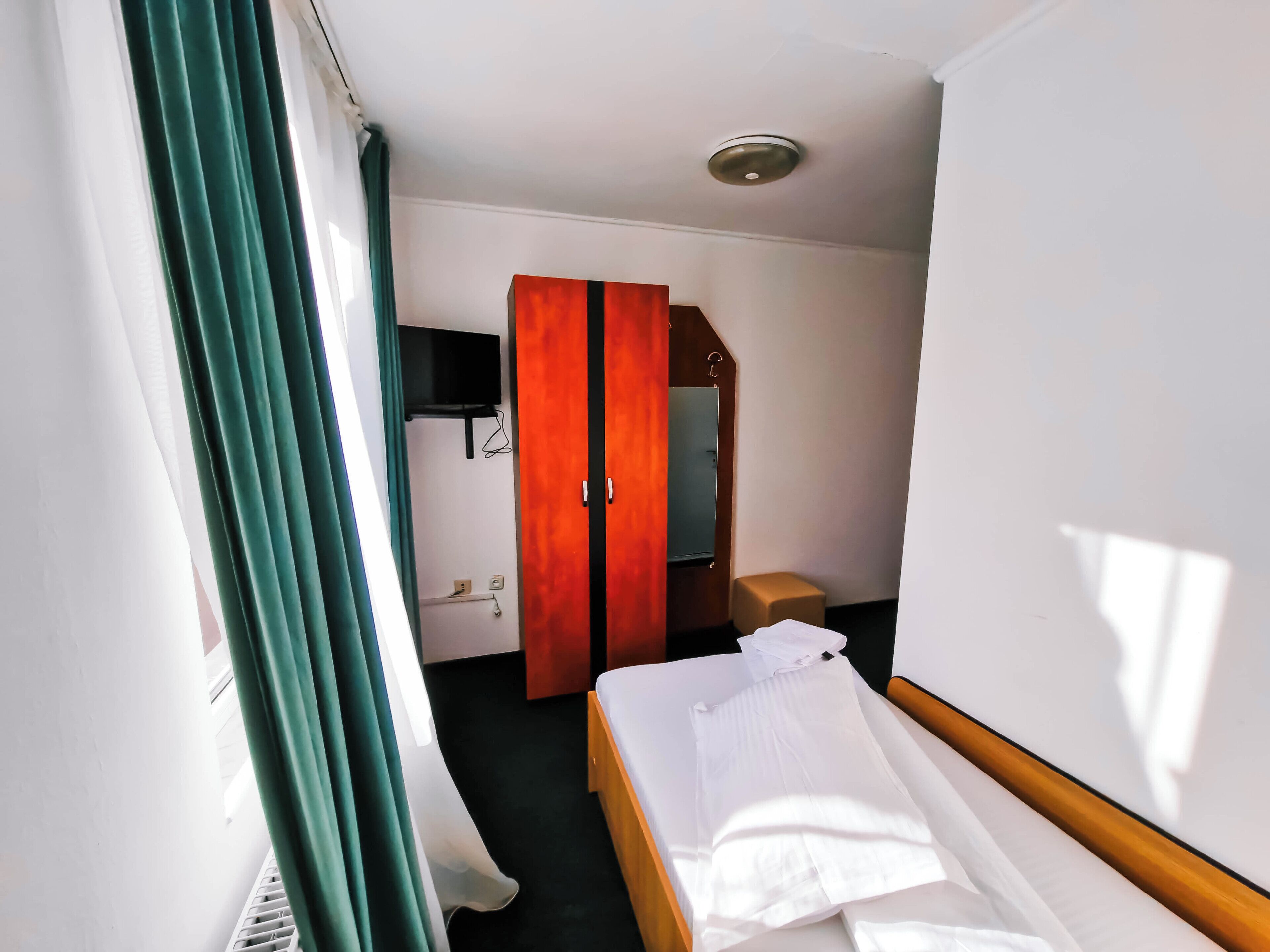 A hotel room with a bed, a wardrobe, a television mounted on the wall, and a small stool.