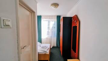 A hotel room with a bed, a bench, a wardrobe, and a window with curtains.