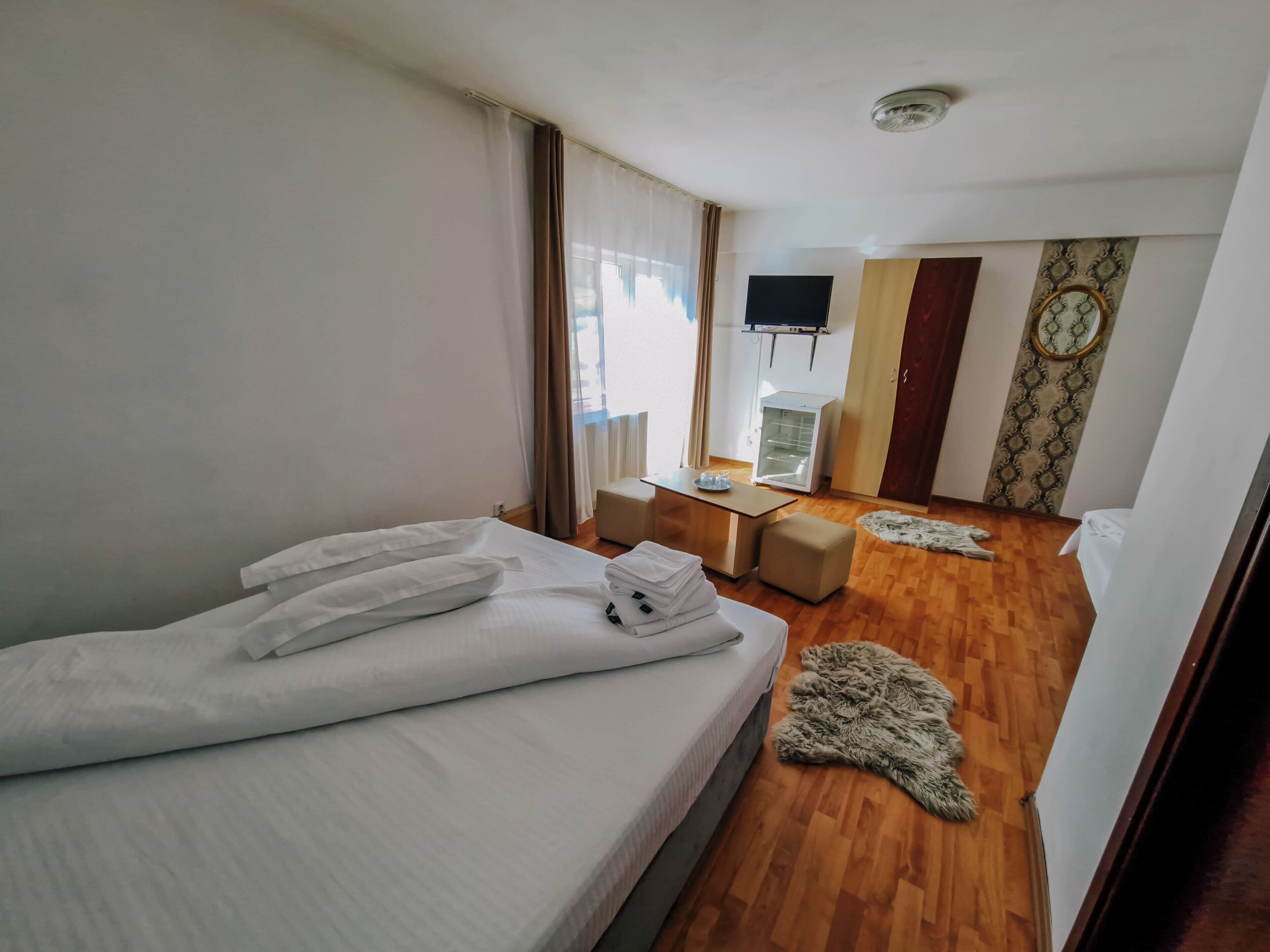 Een hotelkamer met een bed, een bureau met een flatscreen televisie, een kleine koelkast en een kamerkleed met dessin.