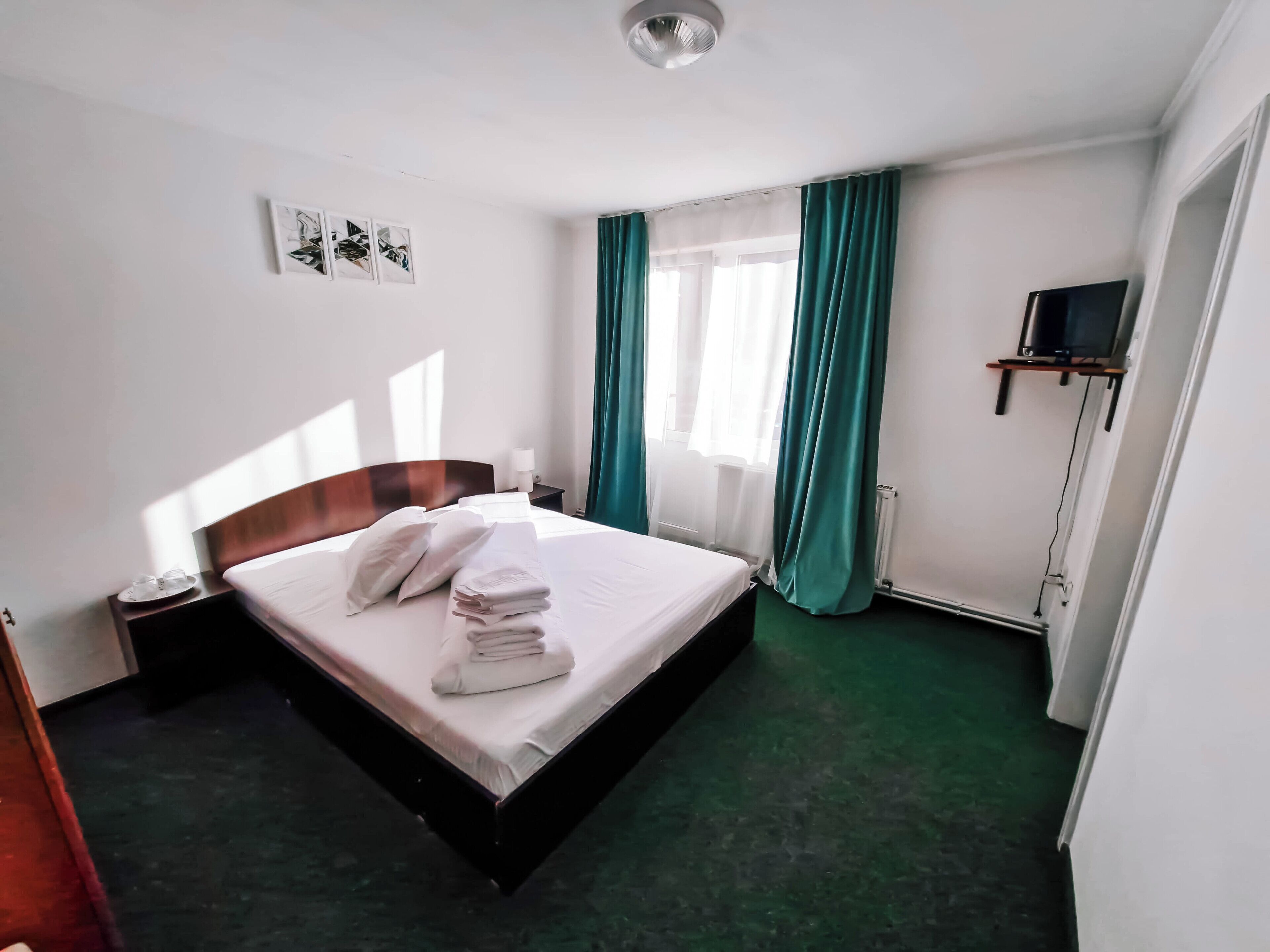 Habitación de hotel con cama, mesita de noche, televisor sobre un mueble y ventana con cortinas.