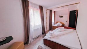 Ein Hotelzimmer mit Bett, einem kleinen Tisch, einem Sessel, einem Spiegel und einem Fenster mit Vorhängen.