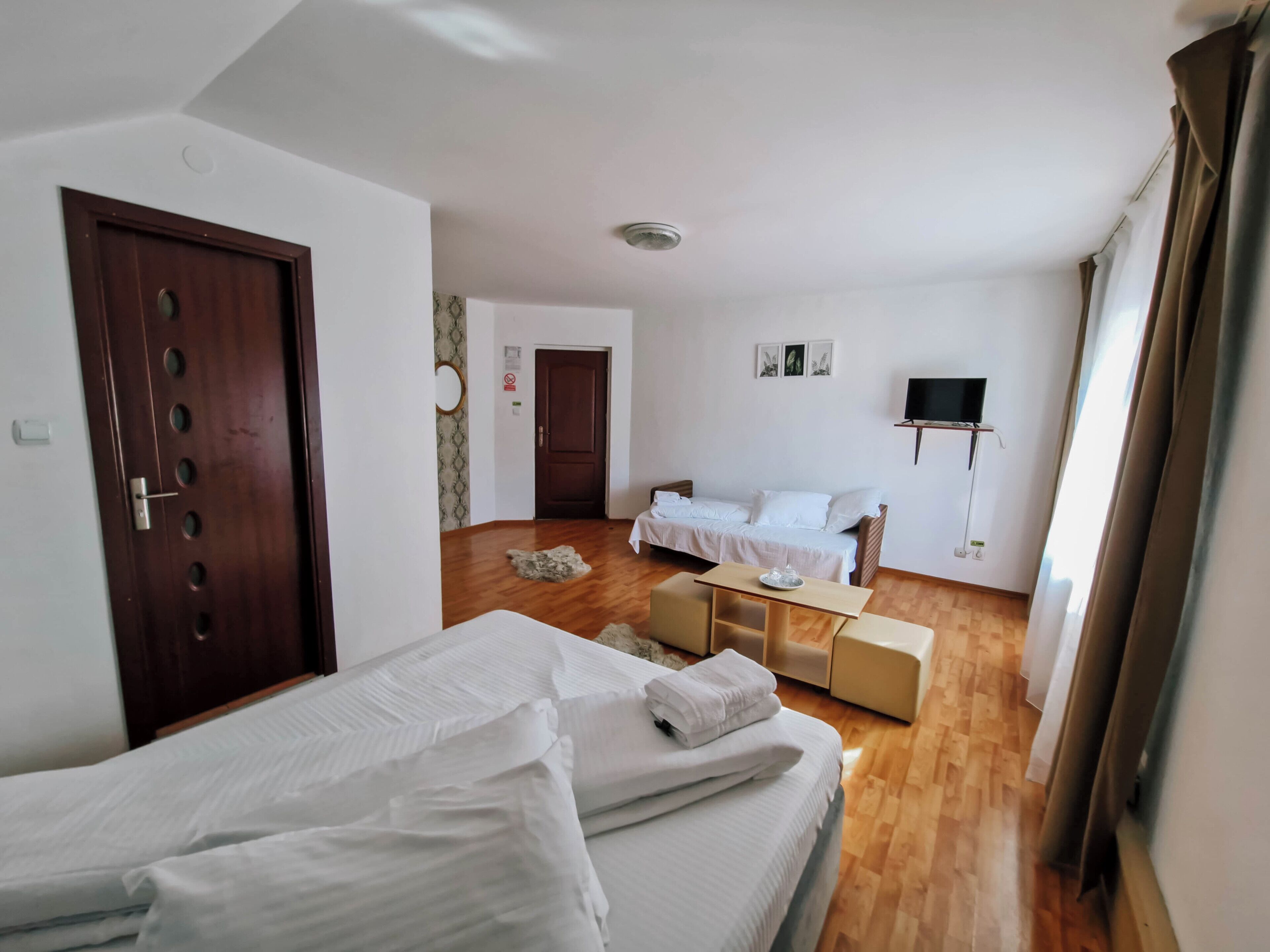 A room with two beds, a sofa, a TV, and a wooden floor.