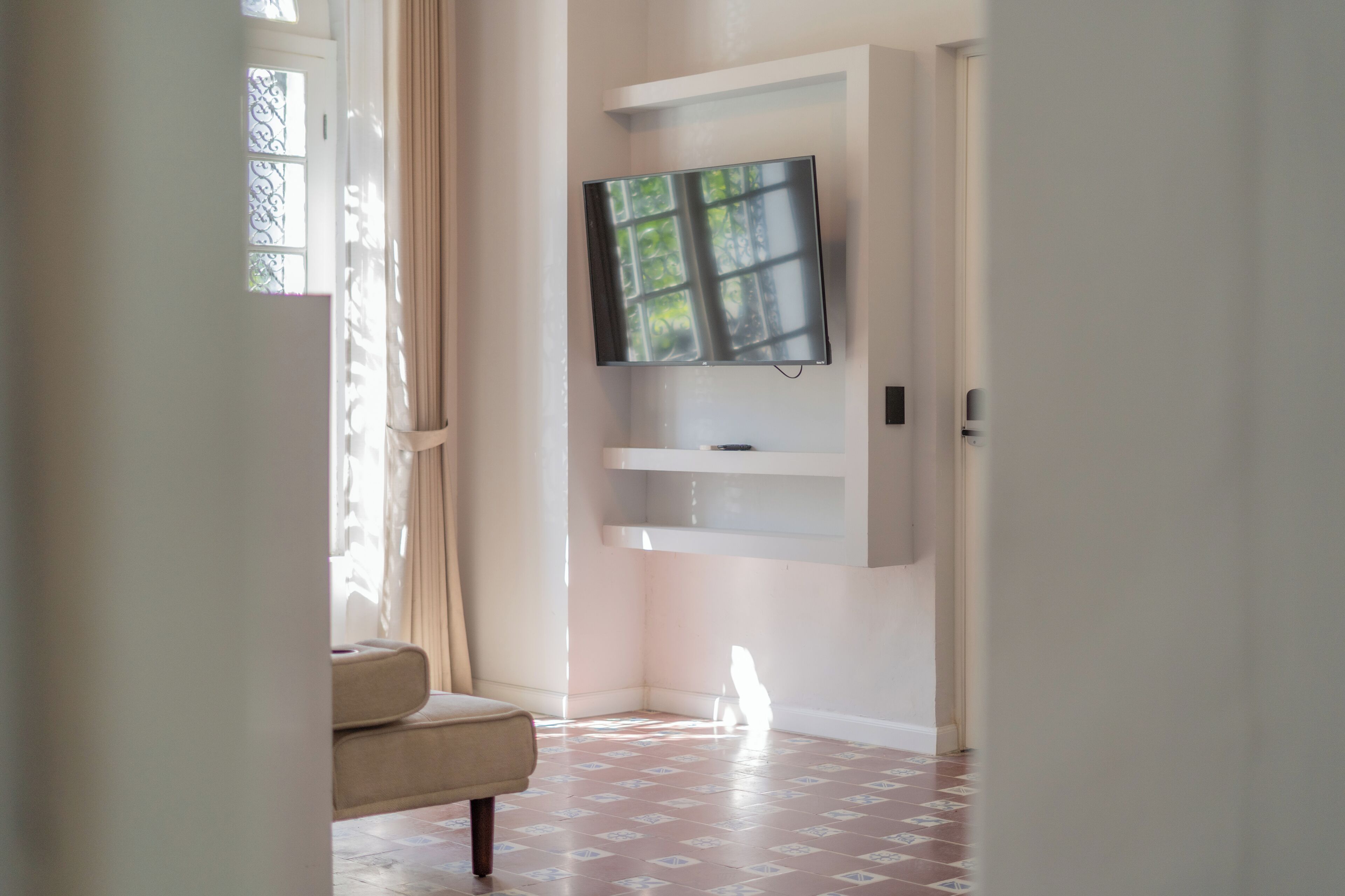 A hallway with a TV mounted on the wall, a chair, and a patterned floor.