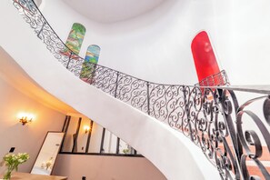 A curved staircase with ornate metal railings, a red object on the railing, and a wall-mounted mirror. - Casa Velasco La Paz (La Paz)