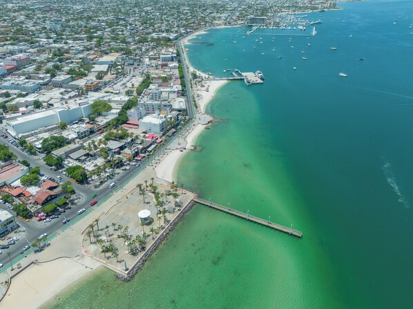 An aerial view of a coastal city with a marina, clear turquoise waters, and a long pier extending into the sea. - Casa Velasco La Paz (La Paz)