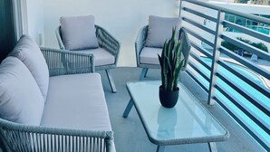 Ein Balkon mit Korbmöbeln, einem Glastisch und einem Blumentopf.