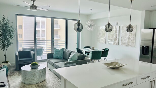 Eine moderne Küche mit einer zentralen Kochinsel, einem Essbereich mit grünen Stühlen und einer großen Schiebeglastür, die auf einen Balkon führt.