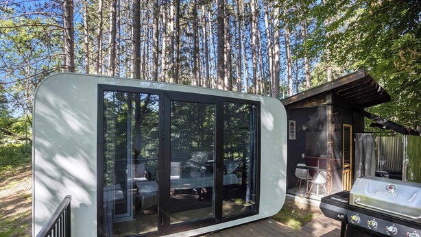 A modern, glass-enclosed cabin with a deck, a barbecue grill, and a patio area. - Hidden Gem Tiny House, Outdoor Screened-In Kitchen (Sears)