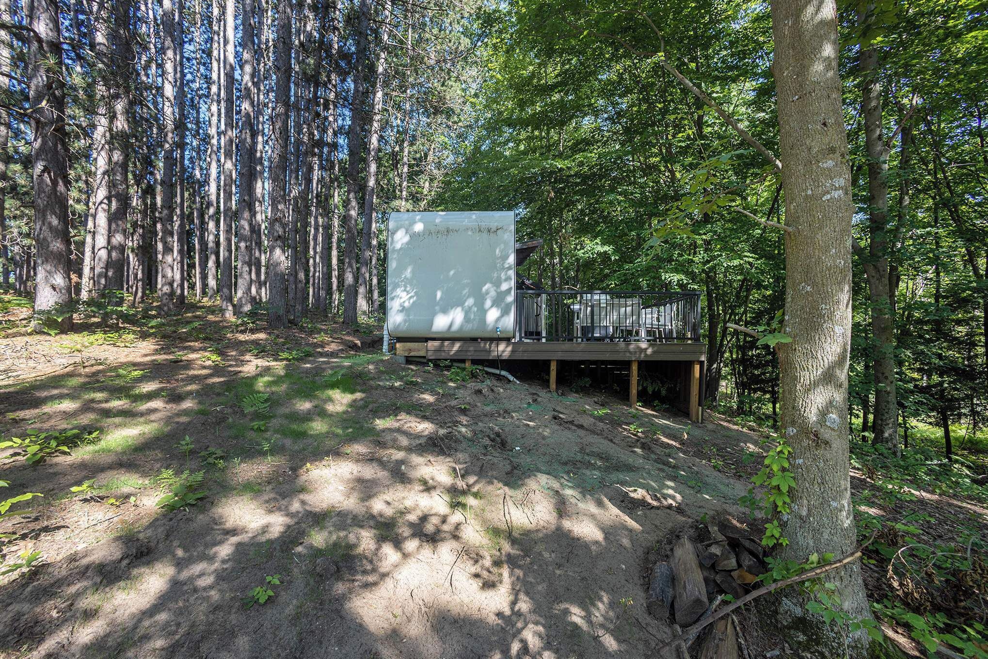 Una cabaña en un bosque con un sendero de tierra que lleva a una terraza de madera.