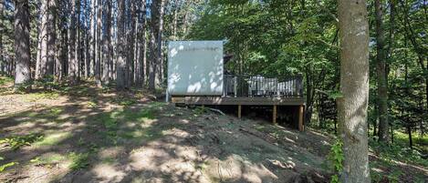 Una cabaña en un bosque con un sendero de tierra que lleva a una terraza de madera.