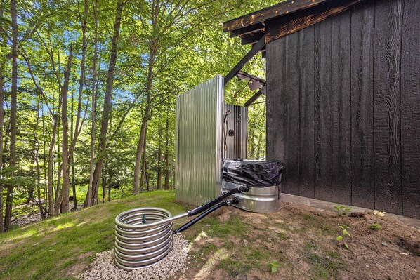A rustic outdoor toilet with a metal structure, surrounded by a forested area. - Hidden Gem Tiny House, Outdoor Screened-In Kitchen (Sears)