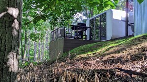 A modern building with a glass facade, a wooden deck, and a staircase leading to a covered area. - Hidden Gem Tiny House, Outdoor Screened-In Kitchen (Sears)