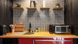 A kitchen with a tiled backsplash, wooden shelves with plants, a sink, a coffee maker, a toaster, and a red cabinet. - Hidden Gem Tiny House, Outdoor Screened-In Kitchen (Sears)
