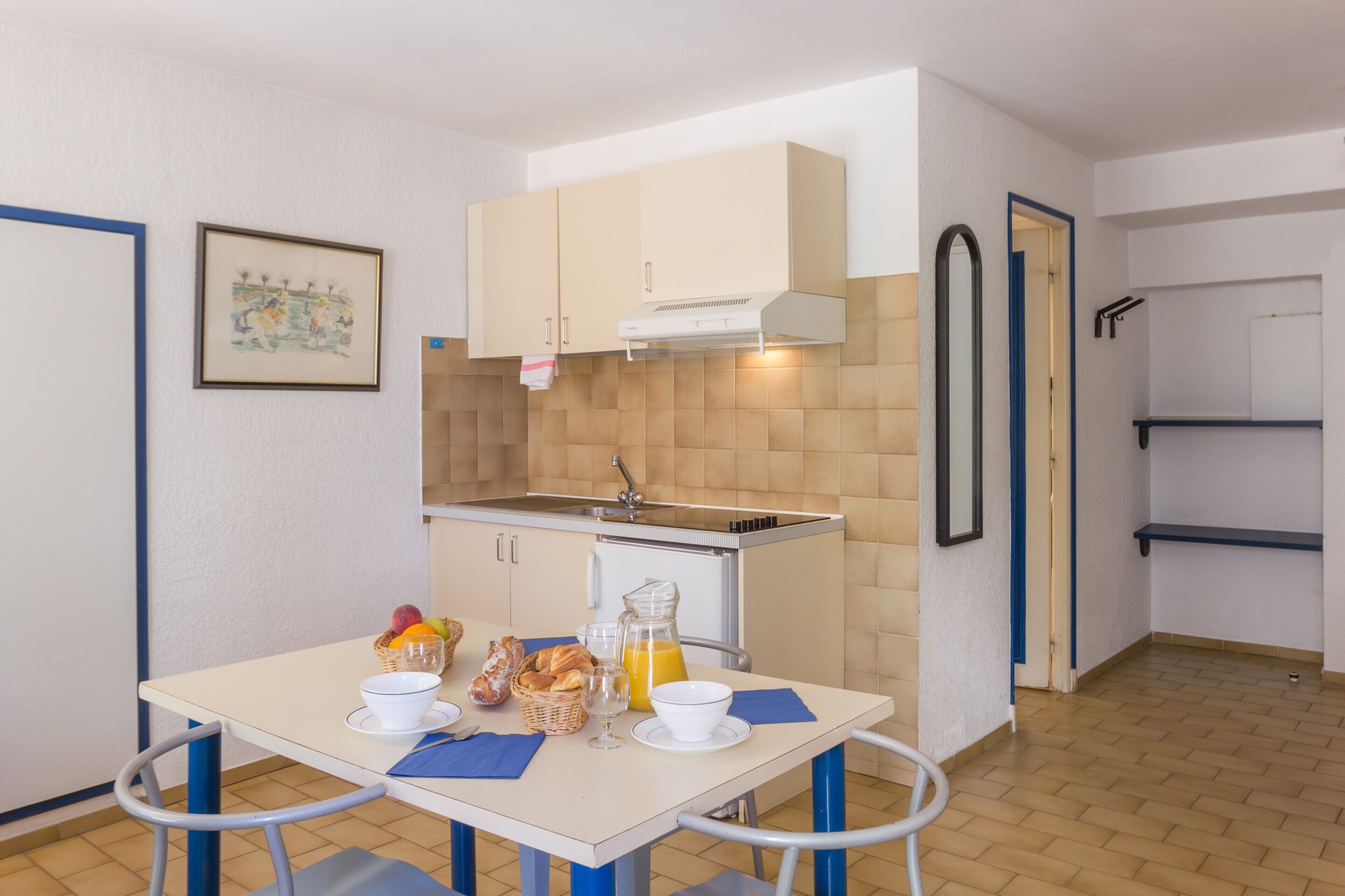 Une cuisine compacte avec un coin repas, comprenant un évier, des placards et un espace pour le petit-déjeuner avec du pain, des fruits et du jus.