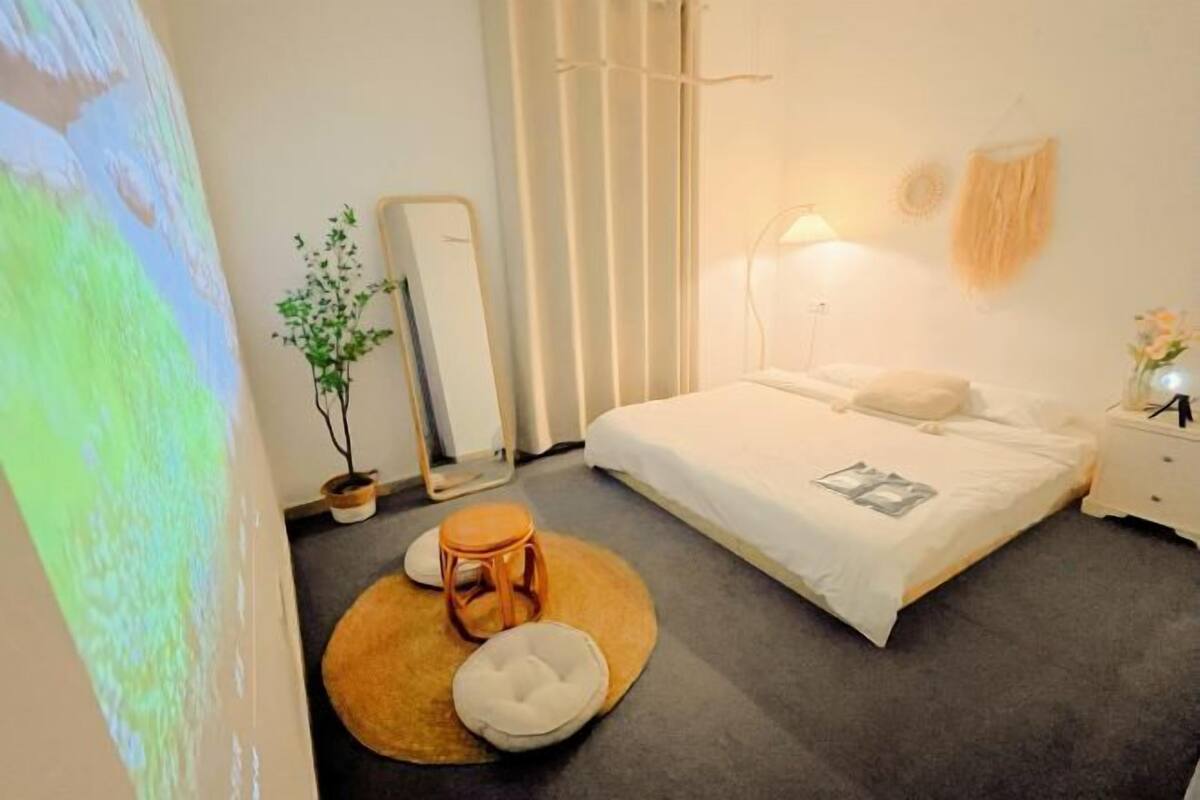 A bedroom with a bed, a nightstand, a mirror, a potted plant, and a round rug.