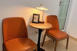 Kaksi oranssia tuolia ja pieni pyöreä pöytä, jonka päällä on lamppu ja kehystetty kuva.