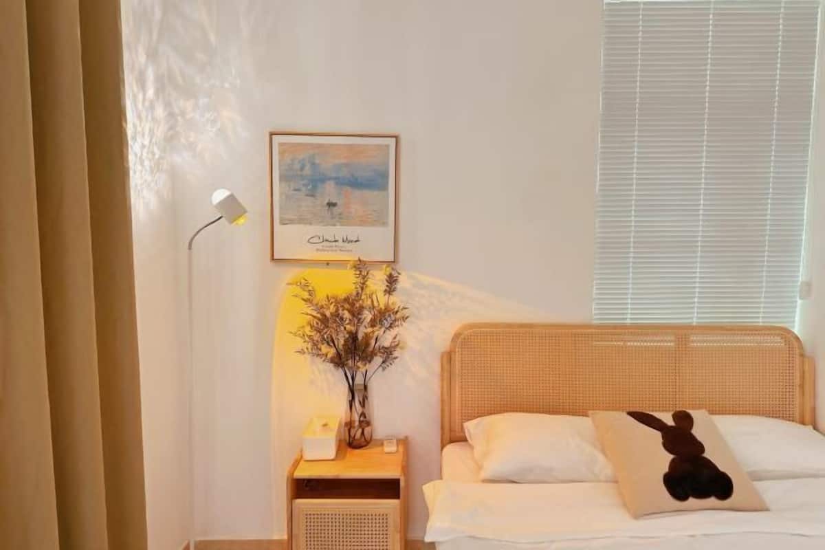 A bedroom with a bed, a bedside lamp, a framed picture, and a vase with dried flowers.