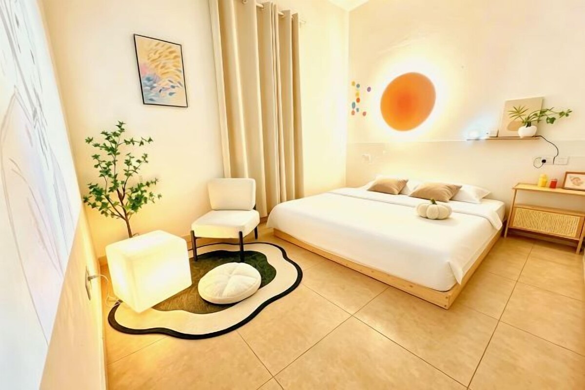 A modern bedroom with a bed, bedside table, chair, and a small plant.