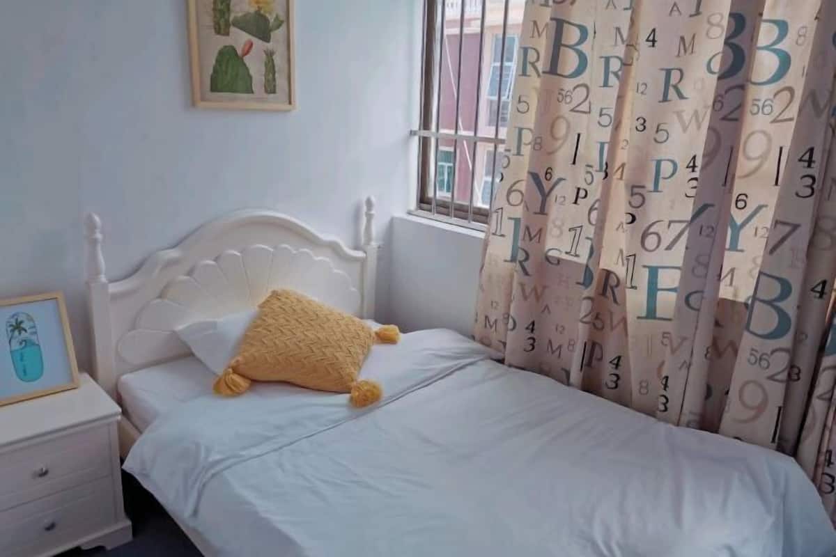 A bedroom with a white bed, a nightstand, a framed picture, and a window with curtains.