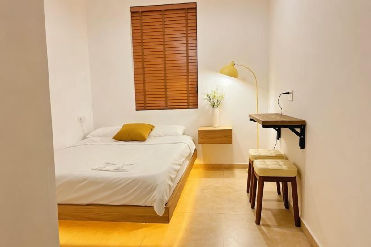 A bedroom with a bed, bedside table, lamp, and a small desk with a chair.