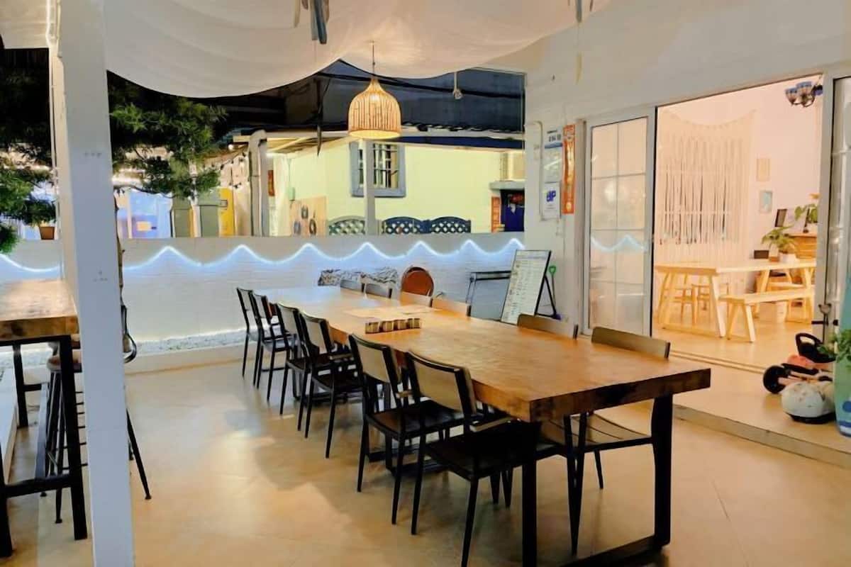 A dining area with a long wooden table and black chairs, a hanging light fixture, and a view of the outside.