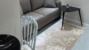 A modern living room with a grey sofa, a small black table, a white chair, and a decorative wall piece. - Luxurious Central Baku Apartment (Baku)