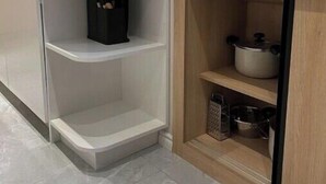 A modern kitchen with white cabinetry, a built-in oven, and a wooden shelf unit with pots and utensils. - Luxurious Central Baku Apartment (Baku)
