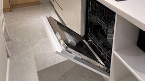 A compact kitchen with a dishwasher, a sink, and wooden cabinets. - Luxurious Central Baku Apartment (Baku)