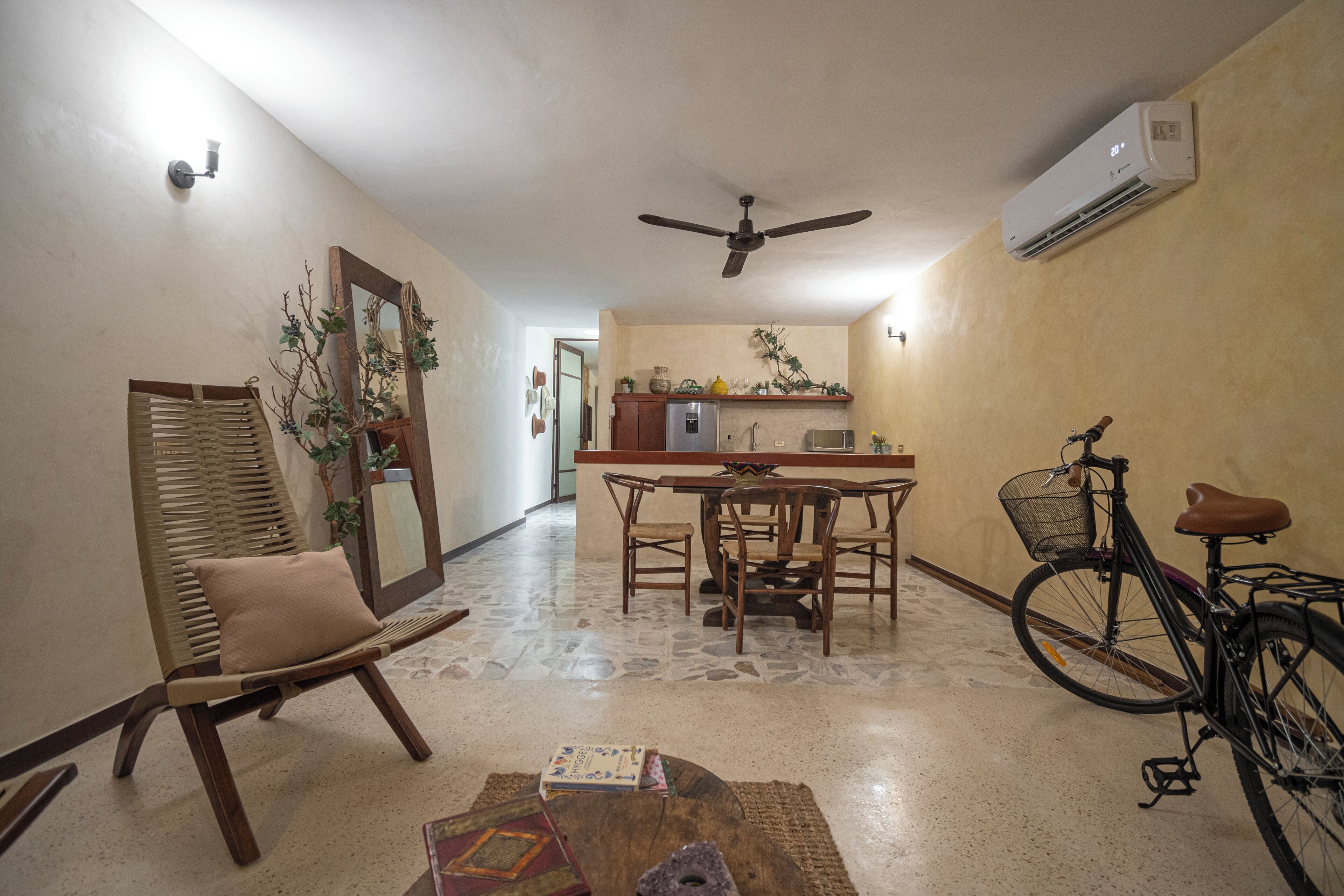 Un espacio habitable compacto con comedor, zona de estar con una silla, una mesa con un libro y una bicicleta.