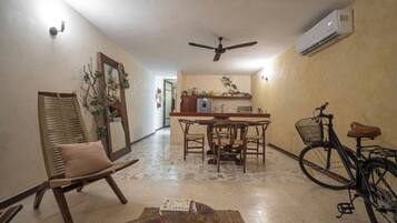 Un espacio habitable compacto con comedor, zona de estar con una silla, una mesa con un libro y una bicicleta.