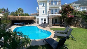 Un bâtiment à deux étages doté d’une piscine, d’un espace extérieur aménagé et d’une structure surmontée d’un toit de chaume.