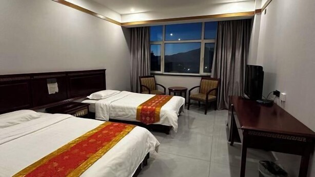 Une chambre d’hôtel avec deux lits, un bureau, une chaise, une télévision et une fenêtre avec des rideaux.