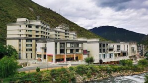 A hotel with multiple buildings, a river in front, and a mountainous backdrop. - Scenic Natural Hotel (Daocheng County)