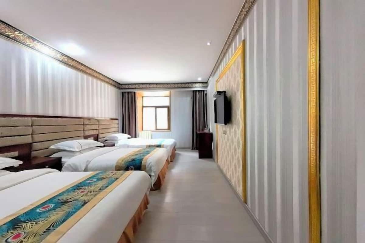 A hotel room with three beds aligned along one wall, a television mounted on the wall, and a window providing natural light.