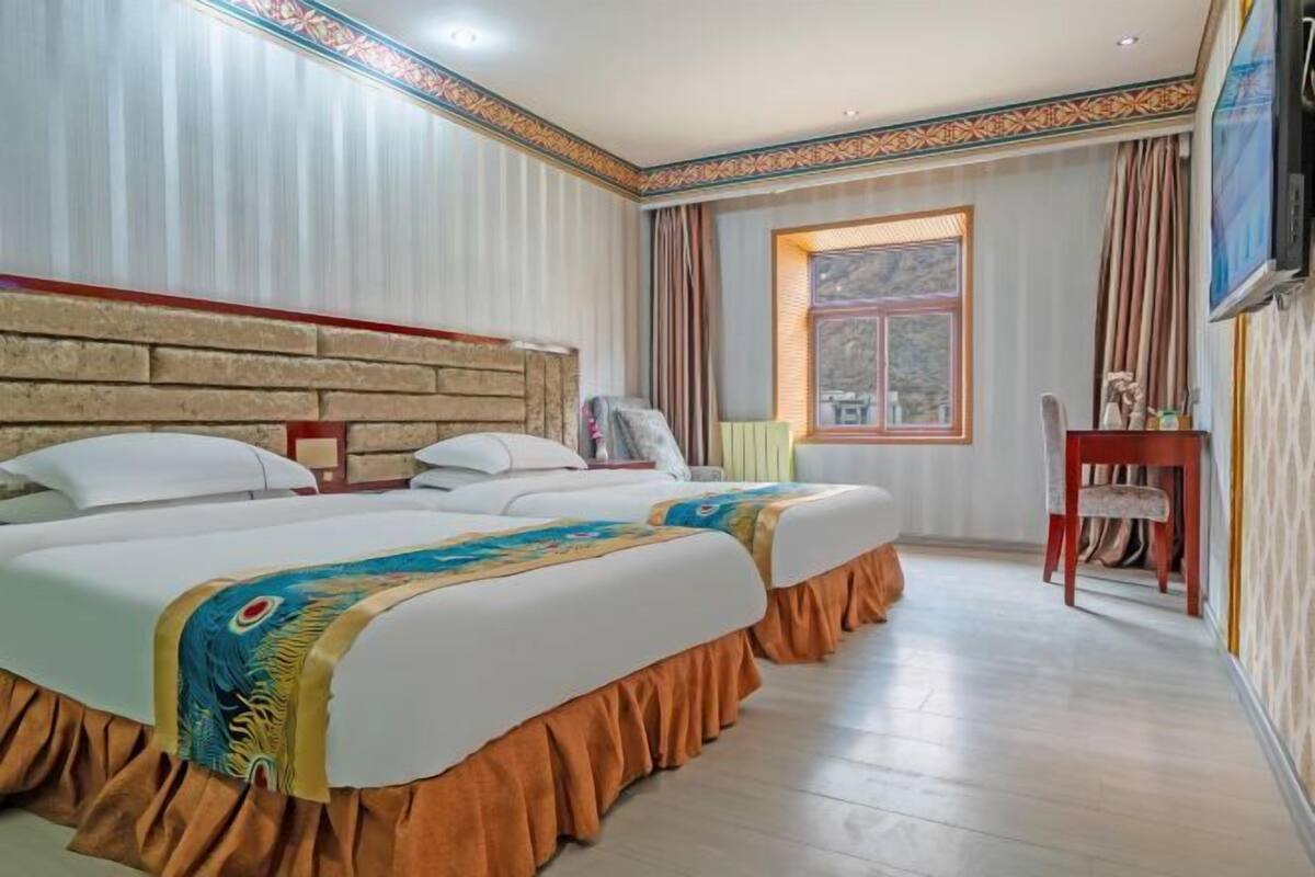 Una habitación de hotel con dos camas, un cabecero de madera, una ventana con cortinas, un escritorio y un televisor.