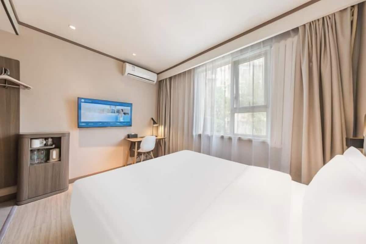 A hotel room with a large bed, a desk with a chair, a television on the wall, and a window with curtains.